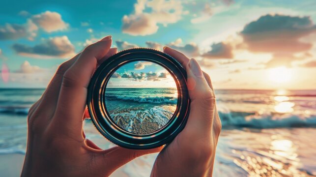 Hands holding camera lens capturing scenic ocean sunset focusing on waves, beach, horizon, photography clarity concept