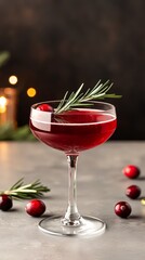 Cocktail glass with cranberry drink and rosemary on a dark background.