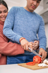 Young couple embracing while cutting vegetables in kitchen