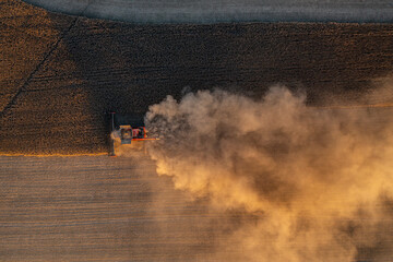 Harvester in field at sunset with dust clouds