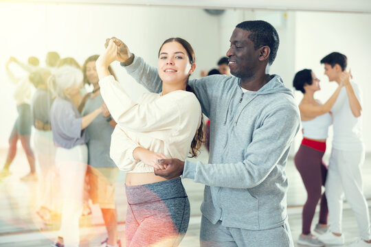 Young smiling girl learning to dance waltz paired with african american man in dancing class..