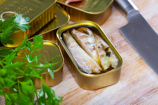 Can of preserved mackerel fish fillets, fresh parsley and garlic on wooden background