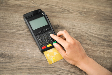 Woman with credit card using payment terminal at wooden table indoors, top view