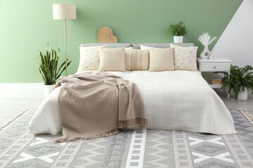 Stylish bedroom interior with large bed, houseplants and decorative elements
