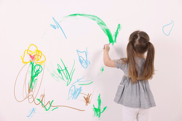 Little child drawing on white wall, back view
