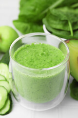 Tasty green smoothie in glass and products on white tiled table, closeup