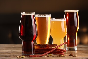 Glasses with different types of beer and snacks on wooden table indoors, closeup