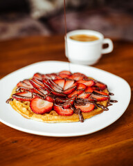 Delicioso waffle con fresa, chocolate y un café americano