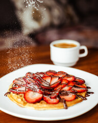 Waffle de fresas con chocolate y una taza de café americano
