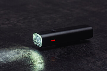 Small black bicycle light with a beam of light, rests on a dark table.