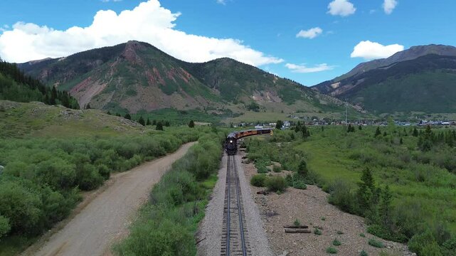 Scenic narrow gauge passenger train pulled by a steam engine leaves Silverton, Colorado. In the background are scenic mountains that surround the town.