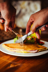 Manos cortando una deliciosa crepa salada de jamón y queso
