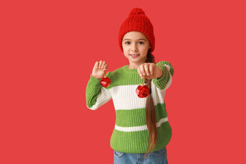Cute little girl in warm hat with Christmas balls on red background