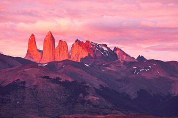 Naklejka premium Torres del Paine in Patagonia, Chile, bathed in the warm glow of a sunrise, with the iconic granite spires illuminated in shades of pink and red against the morning sky.