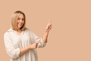 Beautiful young woman with bob hairstyle pointing at something on brown background