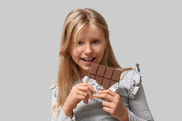 Cute little girl with sweet chocolate bar on grey background