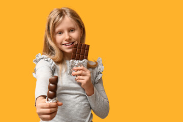 Cute little girl with sweet chocolate on yellow background