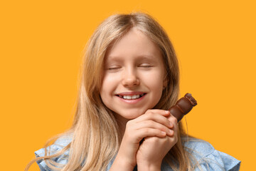 Cute little girl with sweet chocolate on yellow background