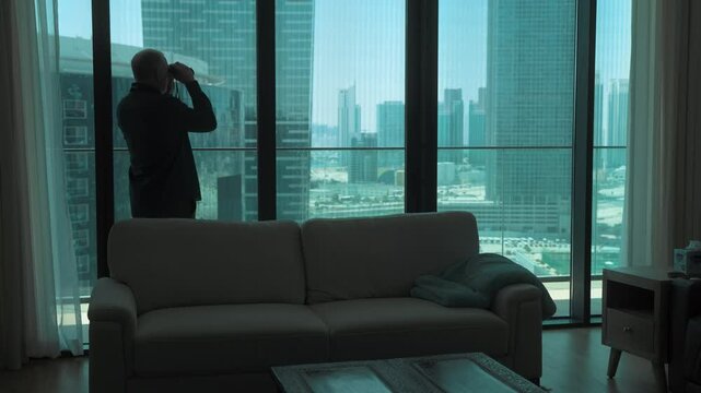Creepy old man spying through his apartment window with binoculars like a peeping Tom