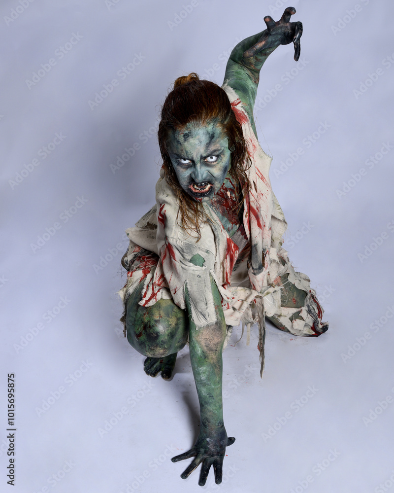 Wall mural portrait of scary female model wearing spooky halloween costume, ripped clothes and fake blood like an undead demon apocalyptic zombie character. Isolated figure, crawling poses dark studio background