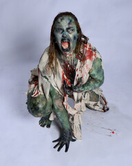 portrait of scary female model wearing spooky halloween costume, ripped clothes and fake blood like an undead demon apocalyptic zombie character. Isolated figure, crawling poses dark studio background