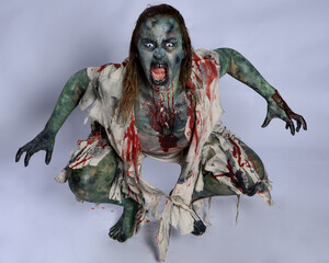 portrait of scary female model wearing spooky halloween costume, ripped clothes and fake blood like...