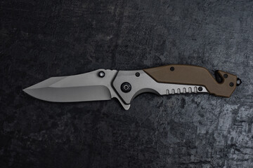 An unfolded tactical military knife with a sharp blade. Tool on dark concrete background.