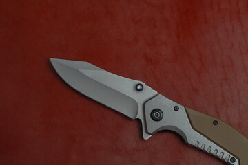 An unfolded tactical military knife with a sharp blade. Tool against the natural leather.
