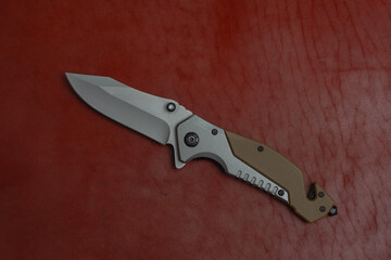 An unfolded tactical military knife with a sharp blade. Tool against the natural leather.