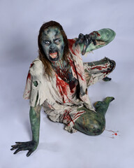 portrait of scary female model wearing spooky halloween costume, ripped clothes and fake blood like an undead demon apocalyptic zombie character. Isolated figure, crawling poses dark studio background