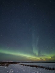 A cold, clear polar night sky with the faint glow of the sun on the horizon and a sky full of stars and aurora lights shimmering

