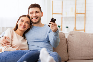 Weekend. Happy Couple Watching TV Relaxing Sitting On Sofa At Home. Selective Focus, Copy Space