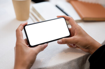 Close-up of a woman holding a smartphone in a horizontal position while sitting at an indoors table.