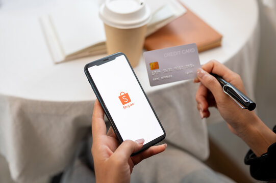 A close-up of a woman holding an iPhone with the Shopee logo on the screen and a credit card.