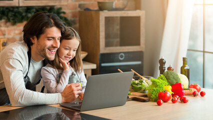 Culinary Blog. Cheerful Young Dad And Little Girl Using Laptop While Cooking In Kitchen Together, Checking Recipes Of Healthy Homemade Food, Browsing Internet, Having Fun At Home, Free Space