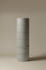 Matte gray cylindrical boxes, stacked upright on beige, soft shadows on the right from left lighting.