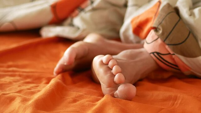 Cozy feet resting comfortably on an orange bedspread bathed in the peaceful morning light