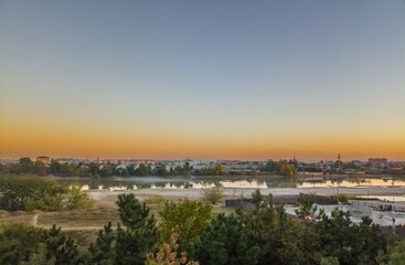 Obraz premium city ​​landscape with calm Kuban river and blue smoke of fires over trees on the opposite bank South of Russia, Krasnodar