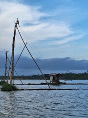 Fototapeta premium Traditional fish cages and a hut in the middle of a lake surrounded by hills, under the sunset sky, in Malang, Indonesia