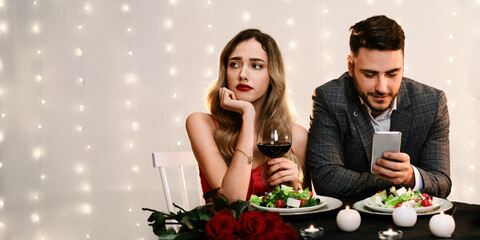 Boring Date. Handsome man using smartphone in restaurant, ignoring his sad girlfriend during romantic dinner