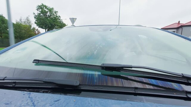 Close-up of car windshield wipers clearing rainwater on rainy day. Safety driving in wet conditions
