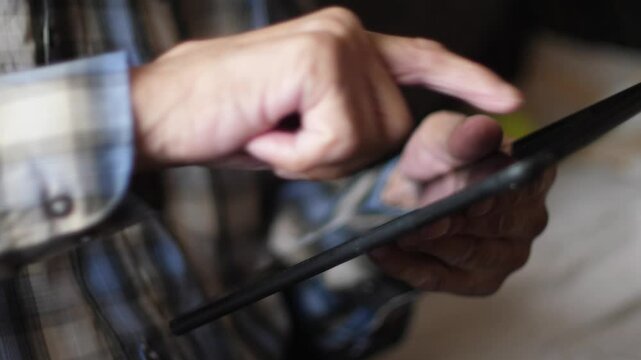 pensioner uses tablet computer browsing web pages, old man's hands press on gadget screen, scrolls news feed and content on social networks, pensioner's leisure