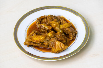 Delicious homemade chicken curry or chicken bhuna on a white plate, placed on light wooden surface.