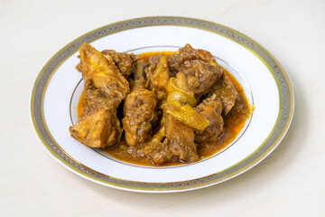 Delicious homemade chicken curry or chicken bhuna on a white plate, placed on light wooden surface. Authentic Bengali cuisine cooked deshi chicken meat.