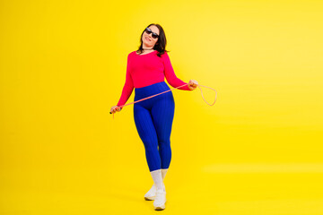 Pretty smiling plump female in sporty top and leggings holding jumping rope in hands