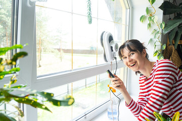 A woman launches a window cleaner robot of the house inside the interior with home plants....