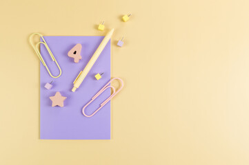 Top view of purple notebook on yellow background. Paperclips, pen, number, shape and pins. School, office wallpaper. Flat lay, copy space.