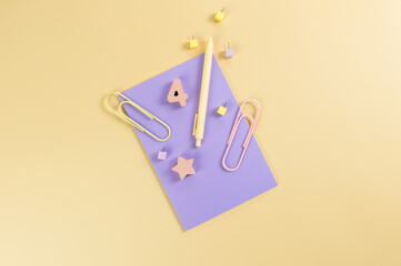 Top view of purple notebook on yellow background. Paperclips, pen, number, shape and pins. School, office wallpaper. Flat lay, copy space.