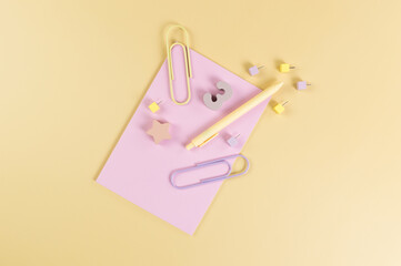 Top view of pink notebook on yellow background. Paperclips, pen, number, shape and pins. School, office wallpaper. Flat lay, copy space.