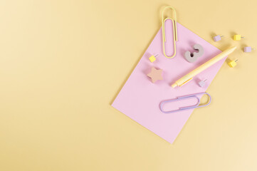 Top view of pink notebook on yellow background. Paperclips, pen, number, shape and pins. School, office wallpaper. Flat lay, copy space.